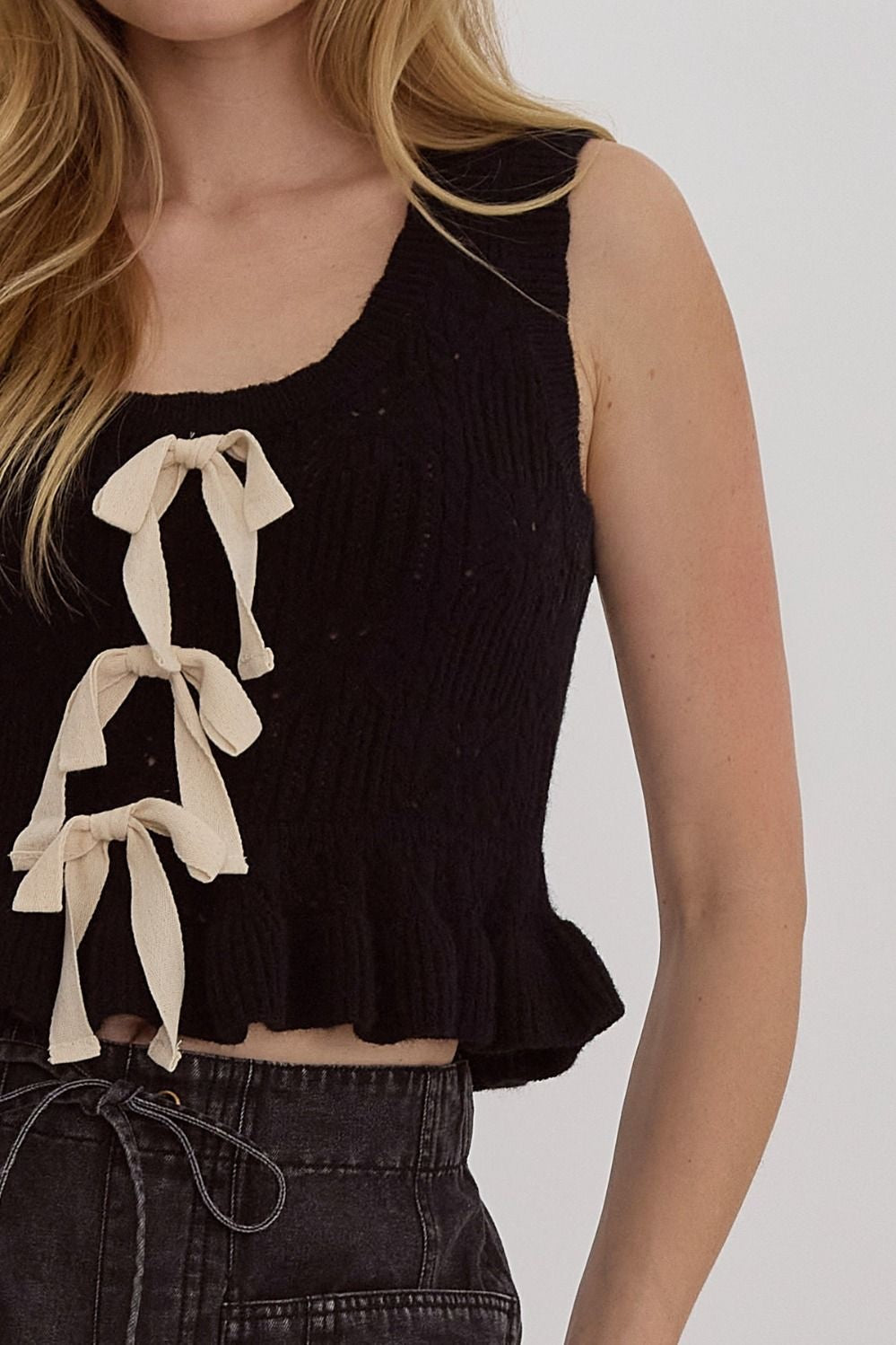 Solid knit scoop neck sleeveless cropped top w/ Ruffle hem. Bow detail at front