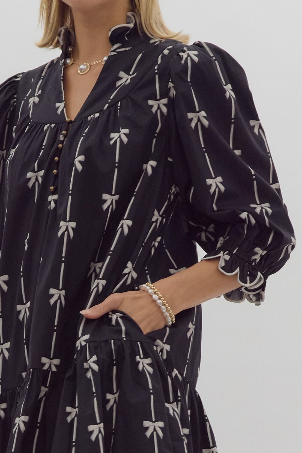 Bow print 3/4 sleeve v neck mini dress w/ button up detail at bust. Ruffled detail at cuff & neckline pockets